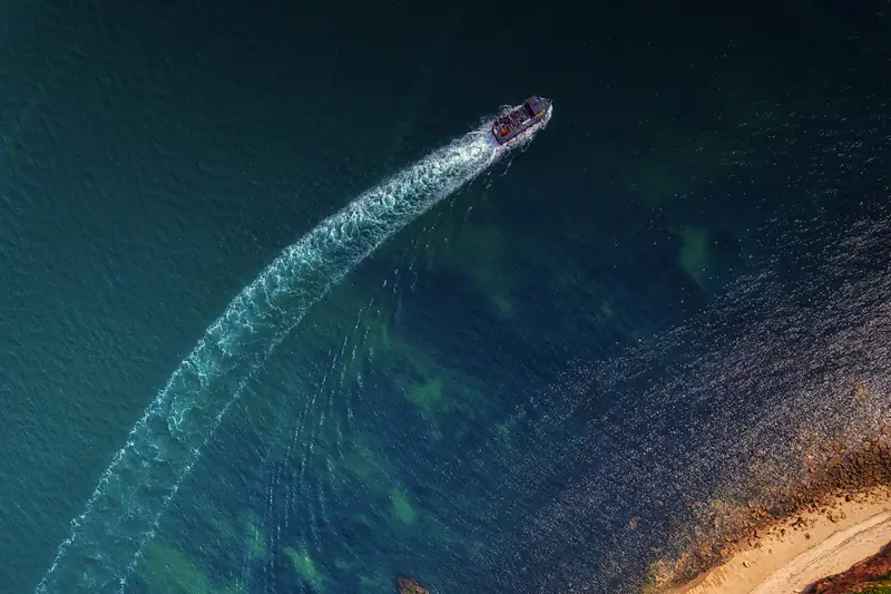 Aerial view of a boat wake along a green and red-cliffed coastline